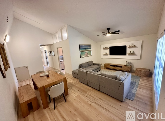 A living room with a grey couch, a wooden table and a ceiling fan.