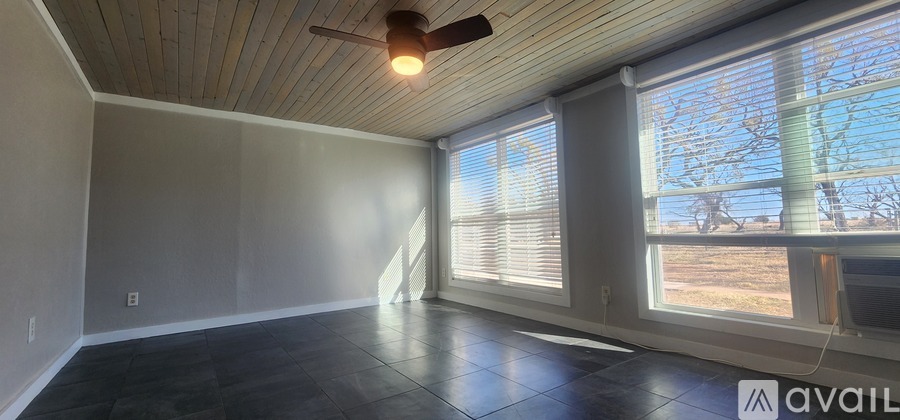 A room with a ceiling fan and large windows.