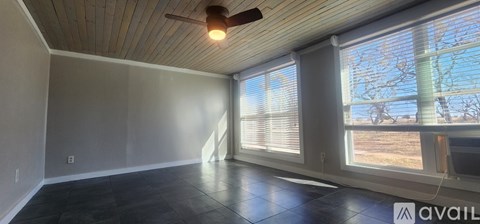 A room with a ceiling fan and large windows.
