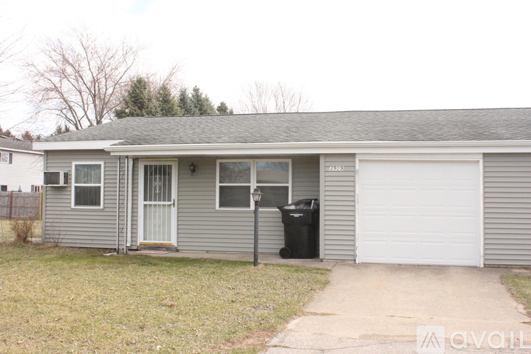 A two-story house with a garage door and a trash can outside.