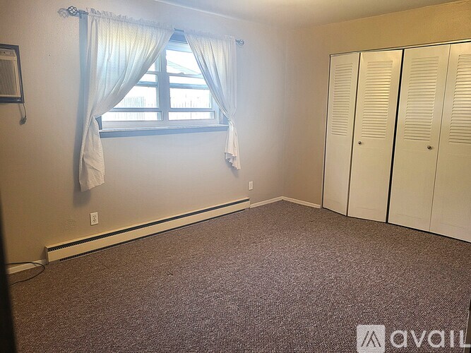 A room with a carpeted floor, a window with curtains, and a wall-mounted air conditioner unit.