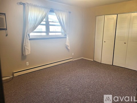 A room with a carpeted floor, a window with curtains, and a wall-mounted air conditioner unit.