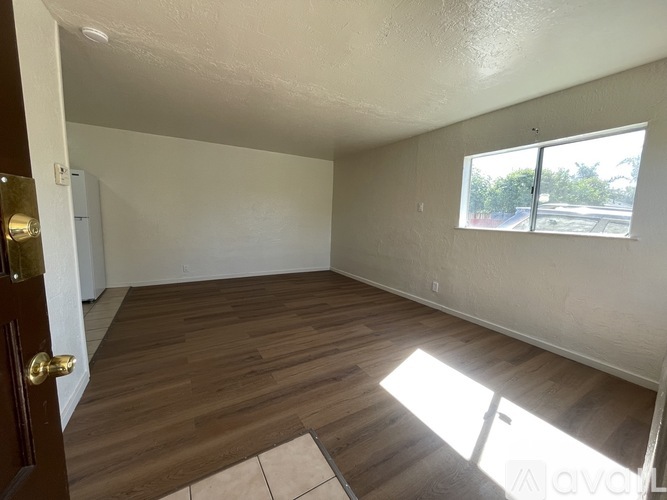 A room with wooden flooring and a window letting in sunlight.