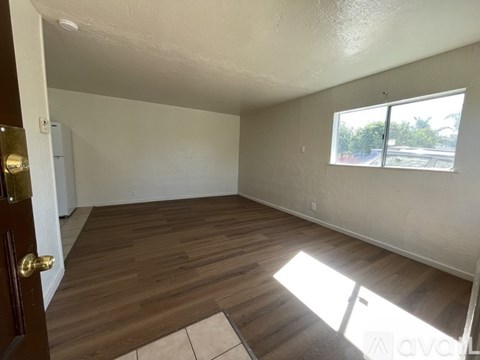 A room with wooden flooring and a window letting in sunlight.