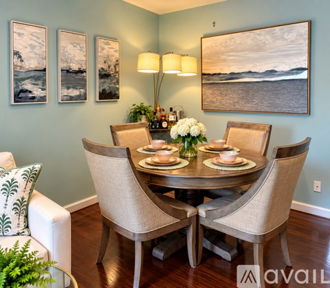 A dining room with a table set for four and a painting on the wall.