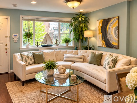 A living room with a white couch, a glass coffee table, and a large window with plants on the windowsill.