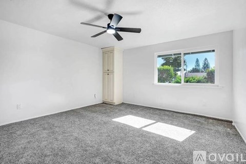 A room with a ceiling fan and a window showing trees outside.