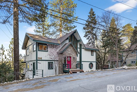 A house with a red door is surrounded by trees and has a snowy ground.