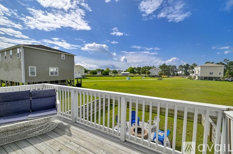 A white deck with a hammock and chairs overlooks a grassy field.