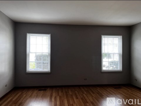 A room with two windows and wooden flooring is available for rent.