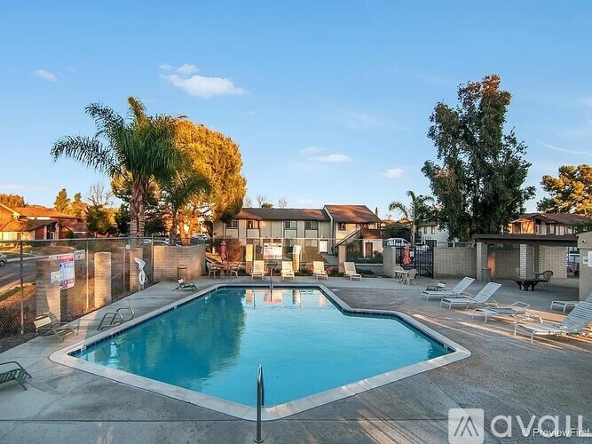 A pool surrounded by chairs and trees with apartment buildings in the background.