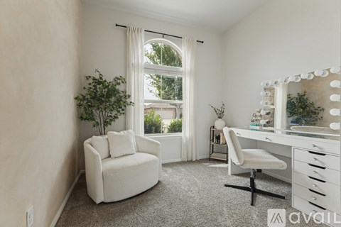 A room with a white chair, desk, and a window with a view of trees.