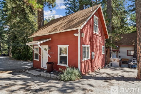 A red house with a white door and windows is surrounded by trees.