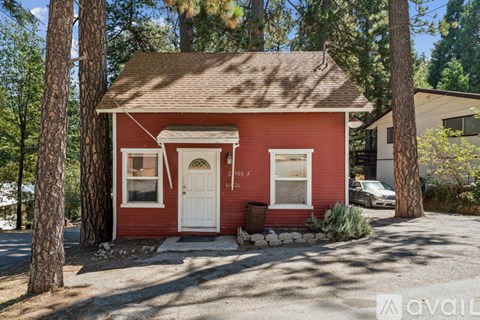 A small red house with a white door and windows is surrounded by trees.