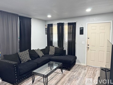 A black sofa with a glass coffee table in front of a white door.