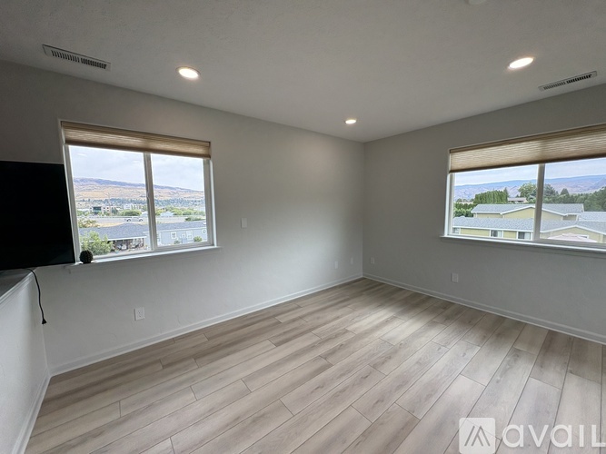 A room with wooden flooring and two windows overlooking a landscape.