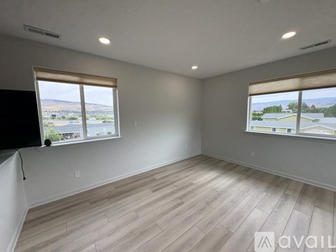 A room with wooden flooring and two windows overlooking a landscape.