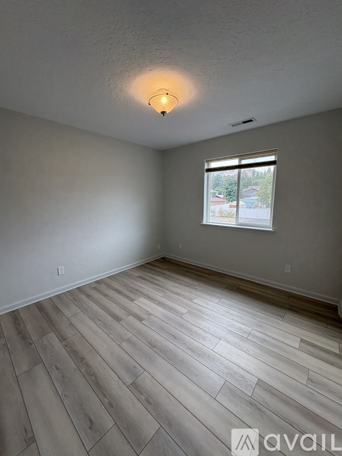 A room with wooden flooring and a window showing a view of a building outside.