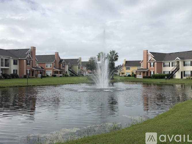 A fountain in the middle of a pond in front of apartment buildings.