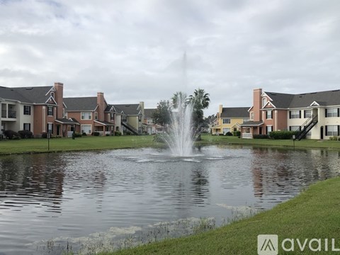 A fountain in the middle of a pond in front of apartment buildings.