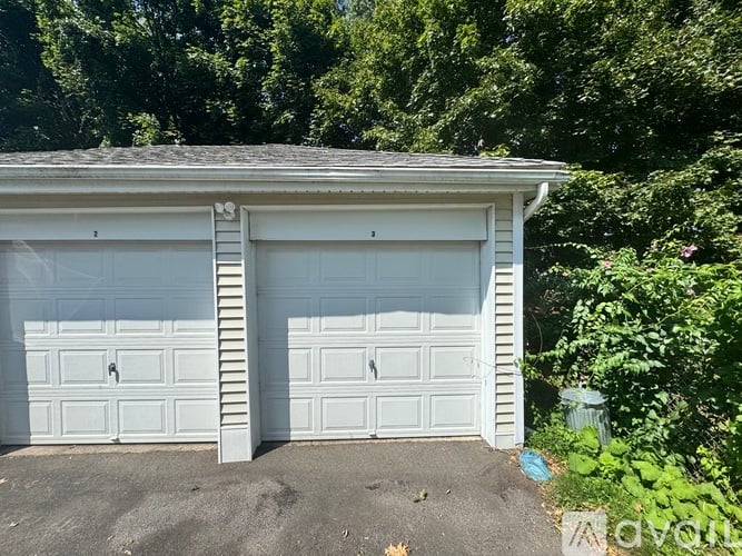A two-car garage with white doors is surrounded by greenery.