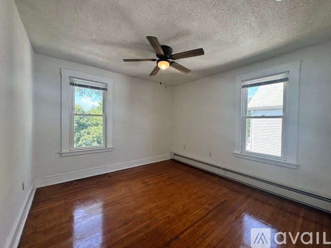 A room with a ceiling fan and two windows.
