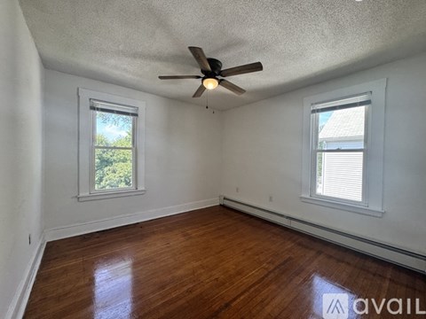 A room with a ceiling fan and two windows.