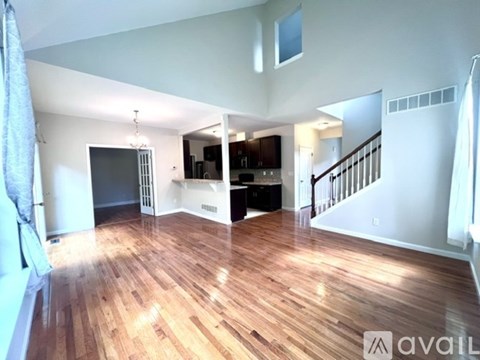A spacious living room with wooden flooring and a staircase leading to the upper level.