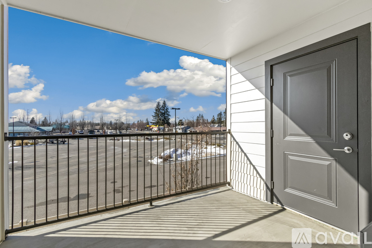 A balcony with a grey door and a metal railing overlooking a parking lot.