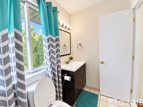 A bathroom with a toilet, sink, and a window with a view of trees.