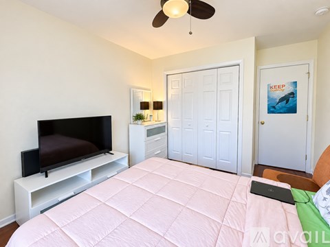 A bedroom with a bed, a television, and a wall-mounted fan.