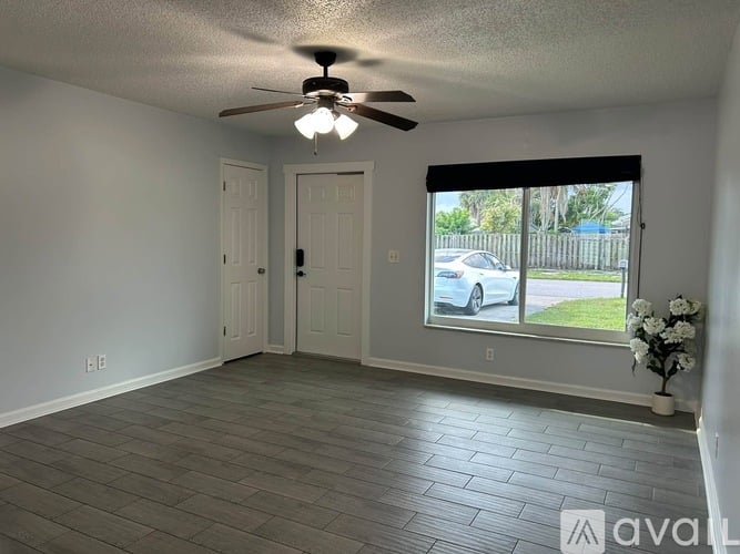 A room with a ceiling fan and a window overlooking a street.