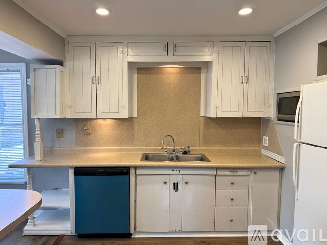 A kitchen with white cabinets and a blue trash can.