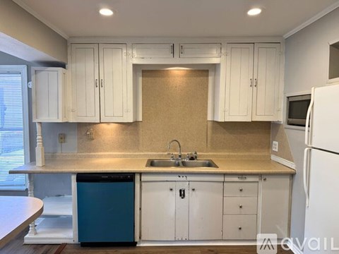 A kitchen with white cabinets and a blue trash can.