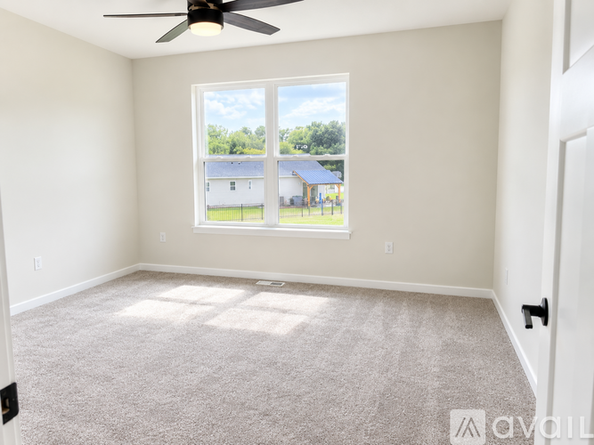A room with a carpeted floor, a ceiling fan, and a large window overlooking a building.