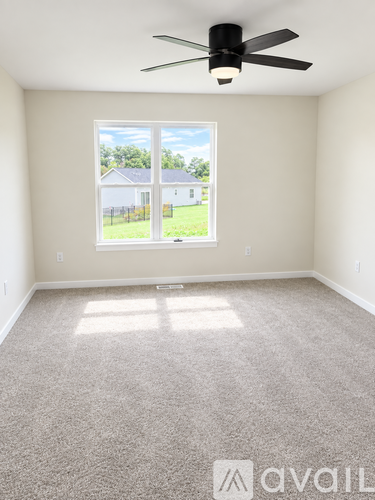 A room with a carpet floor, a ceiling fan, and a window showing a view of a house and trees outside.