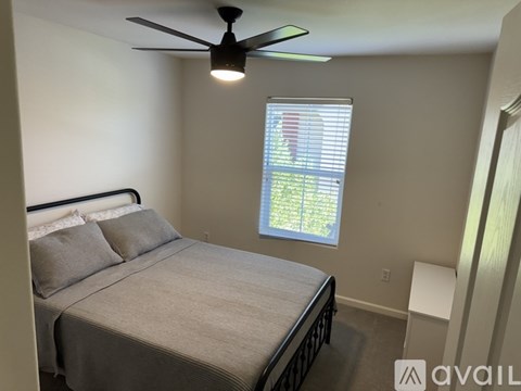 A bedroom with a bed, a ceiling fan, and a window with blinds.