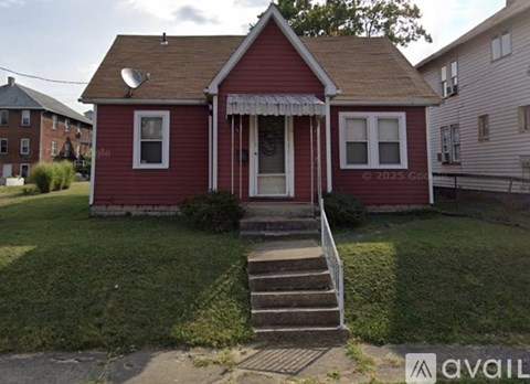 A red house with a white door and windows is surrounded by a green lawn.
