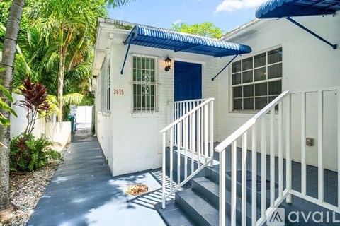 A white house with a blue awning and a white staircase leading to the door.