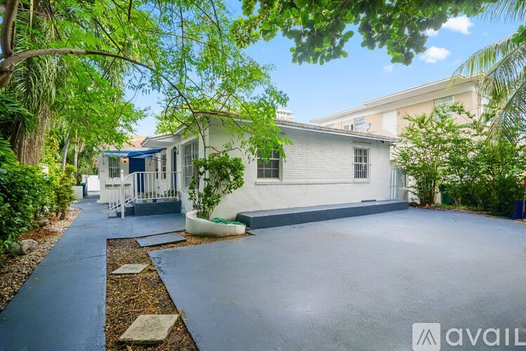 A white house with a driveway and trees in front.