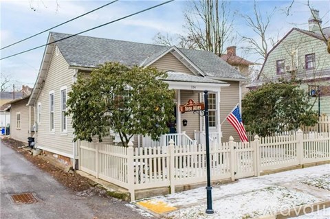 A house with a sign that says "For Sale" is surrounded by a white picket fence.