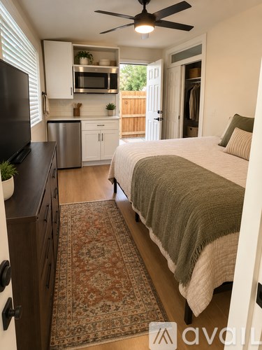 A bedroom with a bed, a ceiling fan, and a kitchen area with a refrigerator, microwave, and stove.