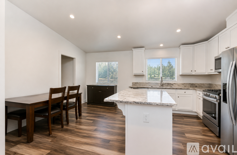 A kitchen with a table and chairs in the foreground and a refrigerator, oven, and microwave in the background.