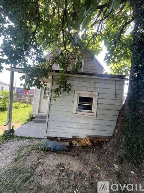 A small house with a white door and a window is surrounded by trees.