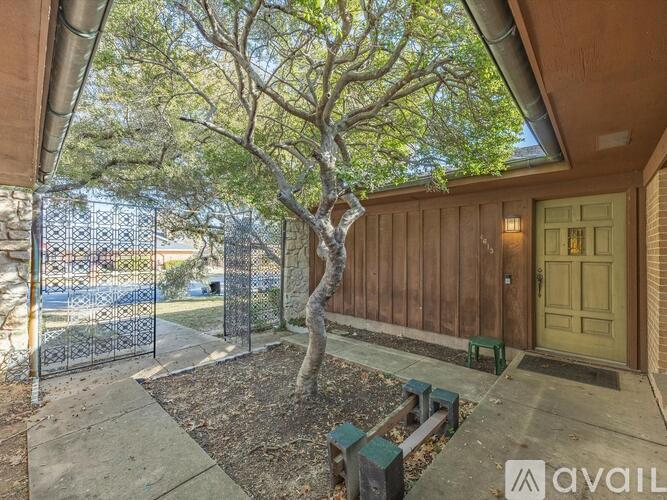 A tree in a pot is in front of a fence and a building.