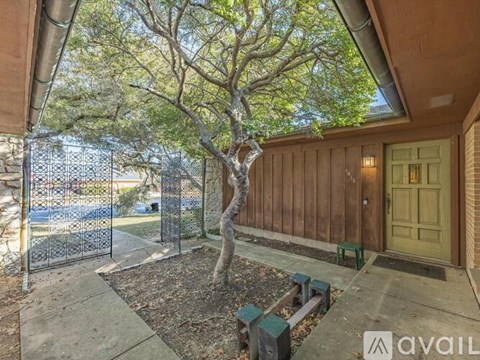 A tree in a pot is in front of a fence and a building.