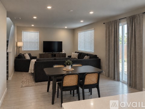 A modern living room with a black sofa, a wooden dining table, and a television.