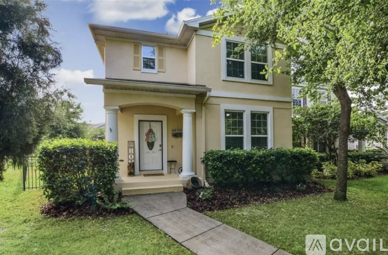 A beige house with a white door and windows surrounded by greenery.