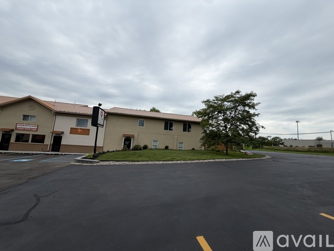 A parking lot in front of a building with a tree and a cloudy sky.