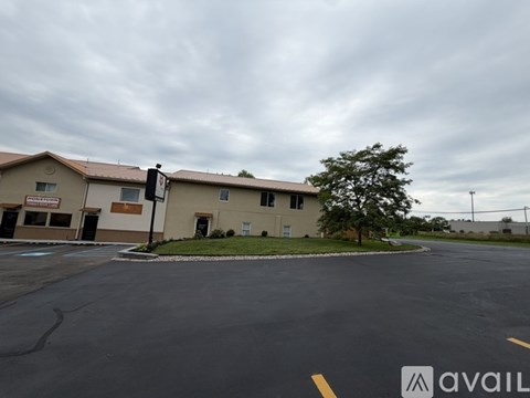 A parking lot in front of a building with a tree and a cloudy sky.
